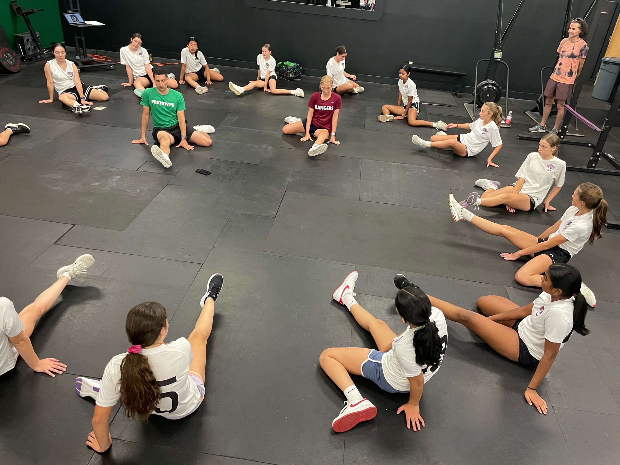 Director of Youth Programs and GM Steve Cimino sitting in a stretching circle with a youth team, co-leading a training session with Junior Coach Caroline Queenan.